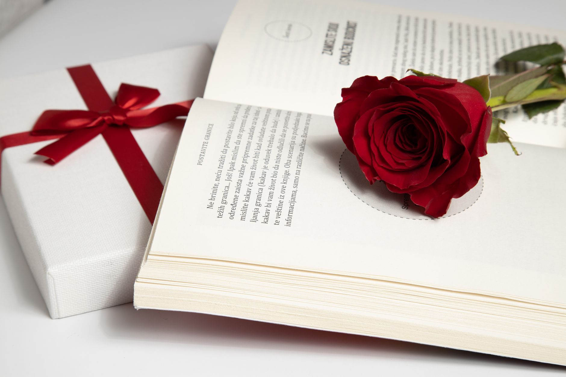 red rose on white book page beside a gift box